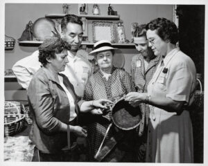 Four women admire a double woven basket displayed at a 1953 craft fair in Asheville, North Carolina, as Goingback Chilotskey, a Cherokee woodcarver, looks on. Hunter Library, Western Carolina University, Cullowhee, SHCG_PhoCF6_10_143 (Photo: Edward L. Dupuy)